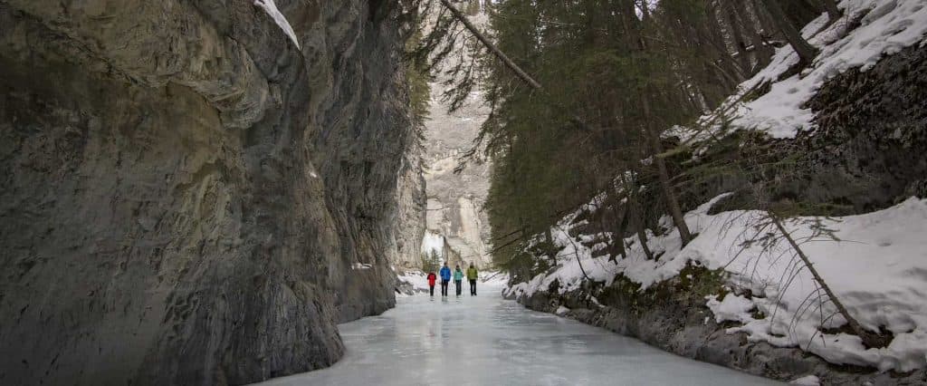 Four people walking on frozen Grotto Canyon, Banff