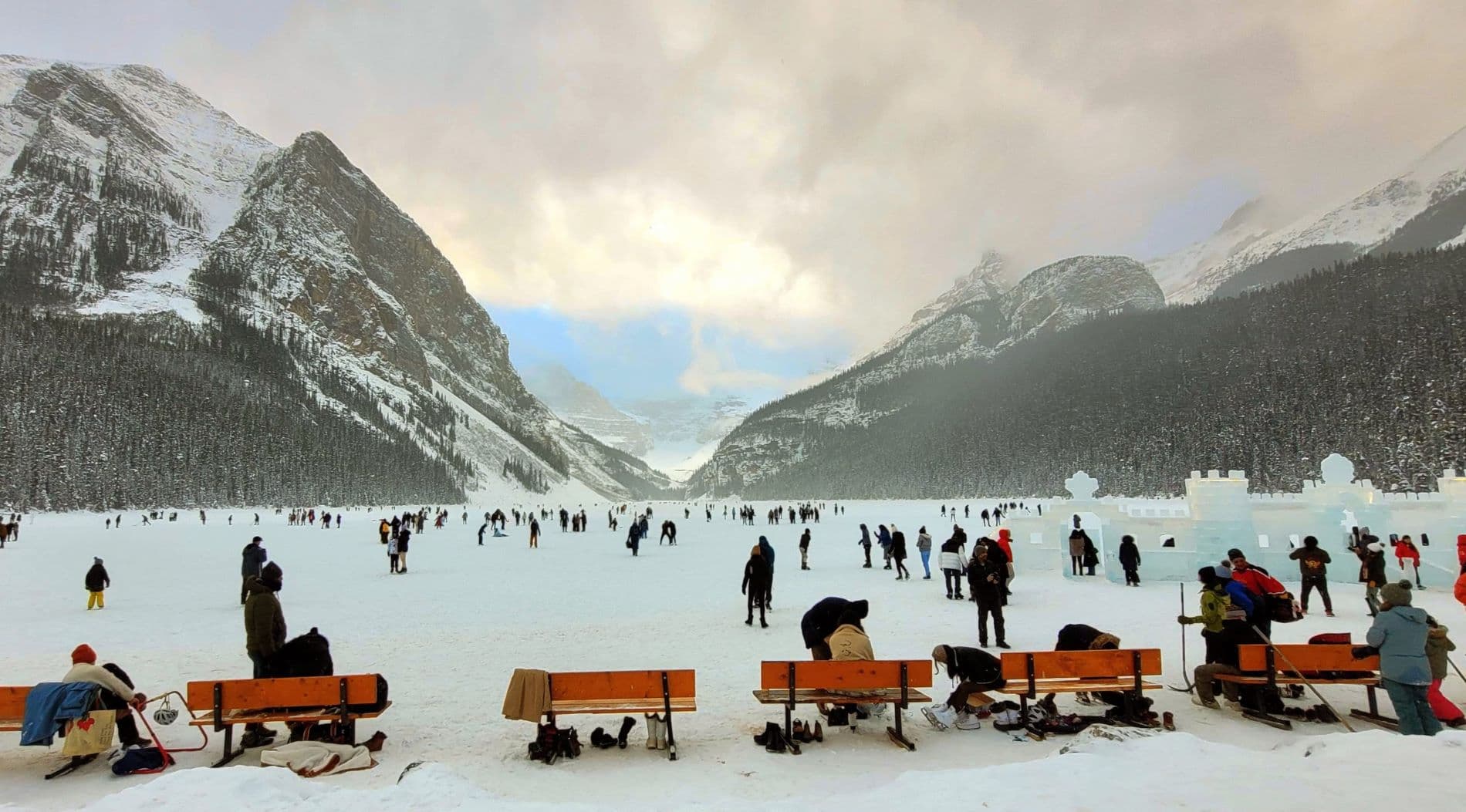 People ice skating and walking on the frozen Lake Louise with mountains in the background